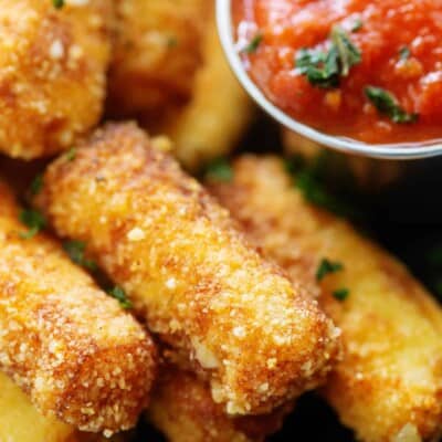 Keto mozzarella sticks on black plate next to marinara.